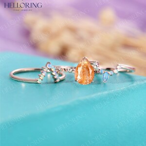 May include: Three gold rings with gemstones. The center ring features a teardrop-shaped sunstone. The two side rings have a curved design with small white opals.