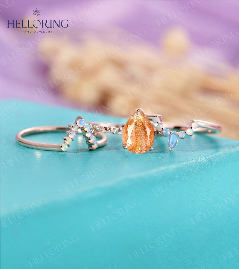 May include: Three gold rings with gemstones. The center ring features a teardrop-shaped sunstone. The two side rings have a curved design with small white opals.