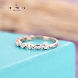 May include: A delicate rose gold band with a row of marquise-shaped diamonds. The band is set on a light blue background.