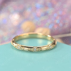 May include: A delicate gold wedding band with a vintage-inspired design featuring small diamonds set in a repeating pattern. The band is shown on a light blue background.