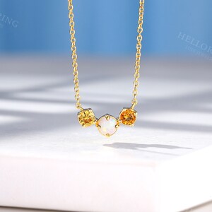 May include: A gold chain necklace with three round gemstones. The center stone is white and the two outer stones are yellow.