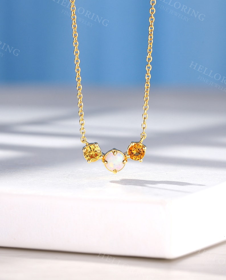 May include: A gold chain necklace with three round gemstones. The center stone is white and the two outer stones are yellow.