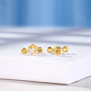 May include: A pair of gold earrings with a small white opal gemstone and two smaller yellow gemstones. The earrings are on a white surface.
