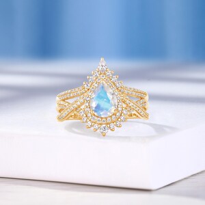 Peut inclure: Une bague en or avec une pierre de lune en forme de poire et un halo de diamants plus petits. La bague a un design d&eacute;licat et complexe avec une double bande.