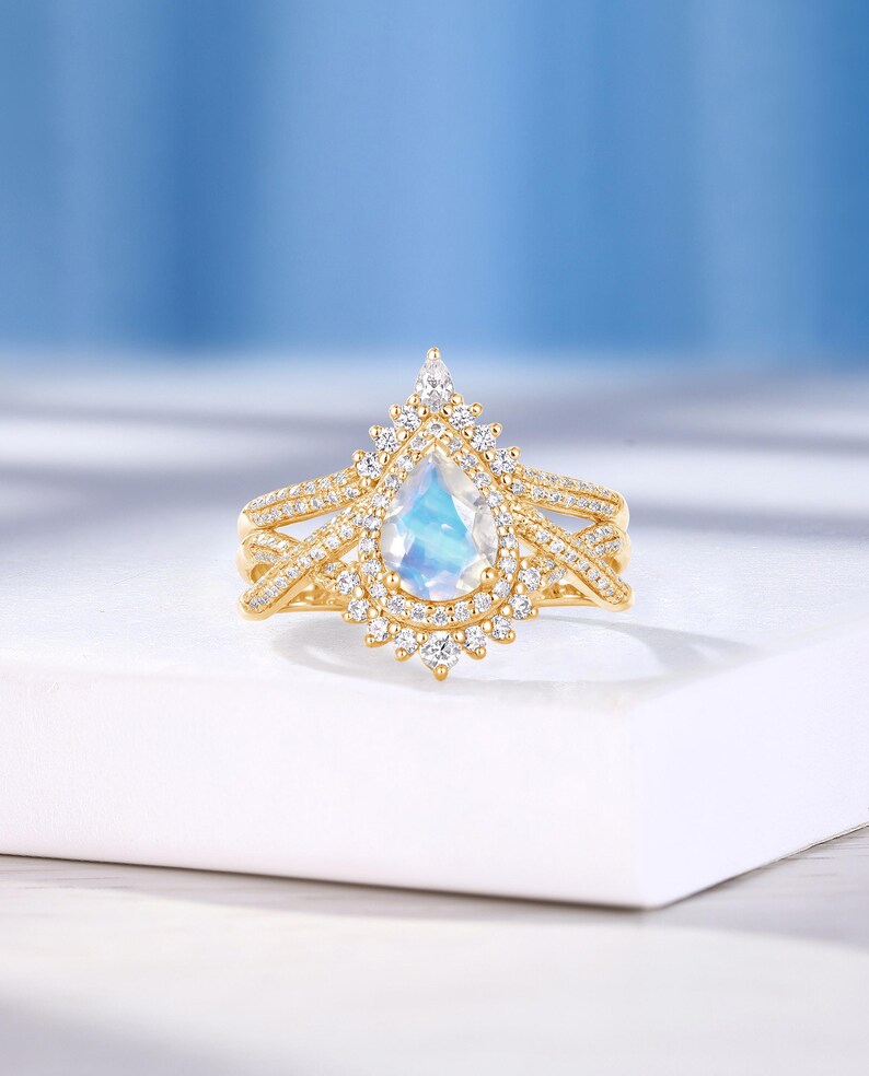 Peut inclure: Une bague en or avec une pierre de lune en forme de poire et un halo de diamants plus petits. La bague a un design d&eacute;licat et complexe avec une double bande.