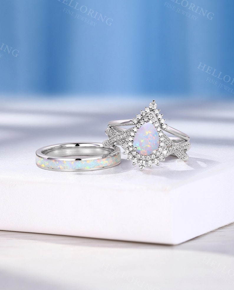 May include: A pear-shaped opal engagement ring set with a halo of smaller diamonds. The ring is set on a silver band and is accompanied by a matching opal and diamond wedding band.