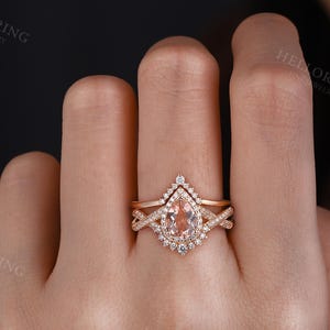 May include: A rose gold engagement ring set with a pear-shaped morganite center stone and a halo of smaller diamonds. The ring is accented with a delicate, twisted band.