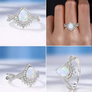 May include: A silver ring featuring a pear-shaped opal gemstone, surrounded by a halo of small, sparkling accent stones. The band has a delicate, twisted design, adding to the ring's elegant appearance. The ring is set against a light blue background.
