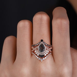 May include: A pear-shaped black diamond engagement ring with a rose gold band and a delicate diamond halo. The ring is set with smaller black diamonds and white diamonds in a unique design.