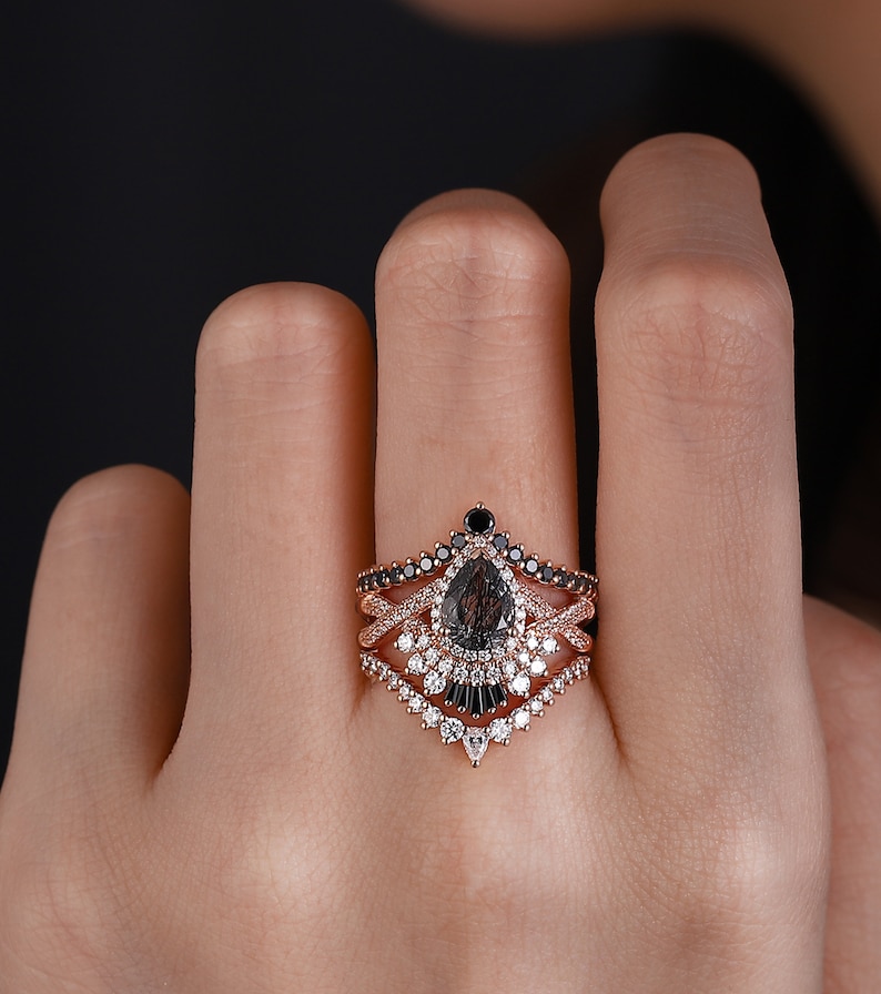 May include: A pear-shaped black diamond engagement ring with a rose gold band and a delicate diamond halo. The ring is set with smaller black diamonds and white diamonds in a unique design.