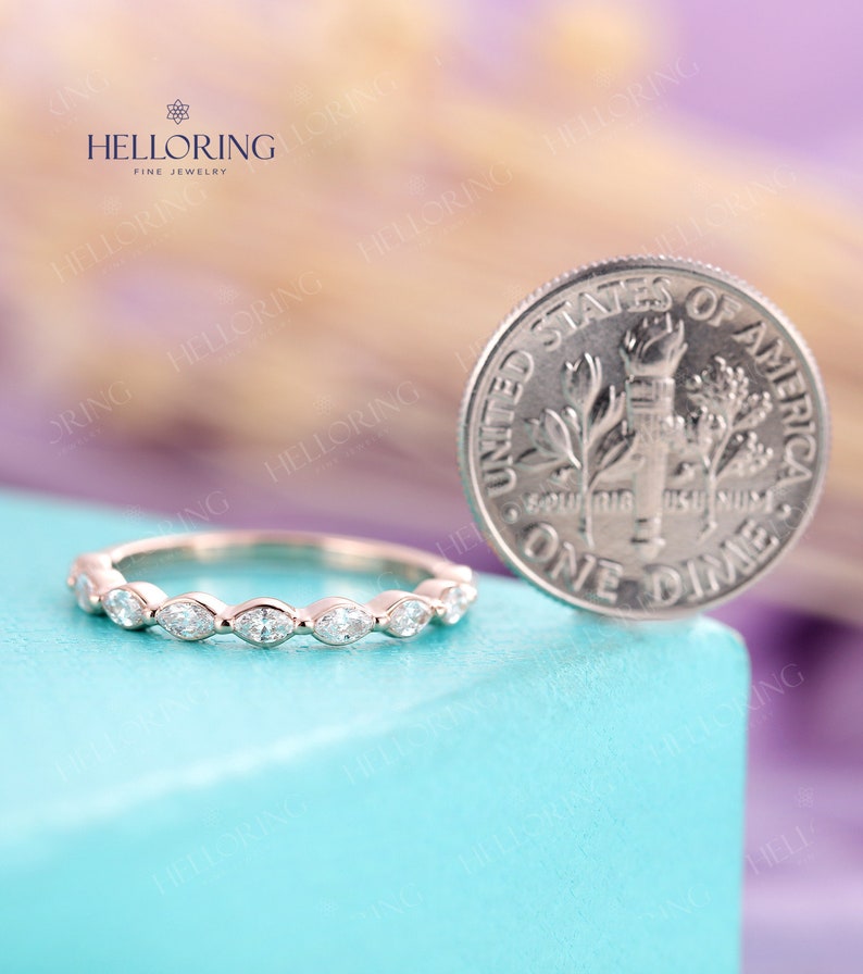 May include: A delicate, thin wedding band with a row of marquise-shaped diamonds set in a scalloped edge. The band is shown next to a US dime for size comparison.