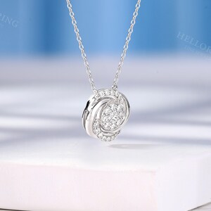 May include: A silver chain necklace with a small, round pendant featuring a cluster of sparkling white diamonds set in a delicate, twisted design.
