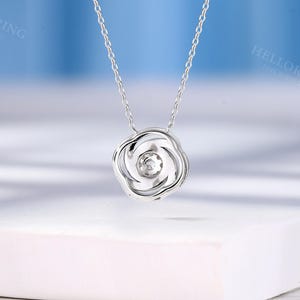 May include: A silver chain necklace with a rose-shaped pendant featuring a small, clear gemstone in the center.