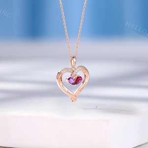 May include: Rose gold heart pendant necklace with a delicate chain. The pendant features a heart-shaped design with a smaller heart inside, holding two gemstones. The names "Mary Ann" and "Jonathan" are engraved on the pendant.