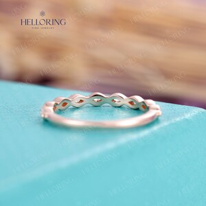May include: A delicate gold band with a row of marquise-shaped gemstones. The band is set on a light blue background.