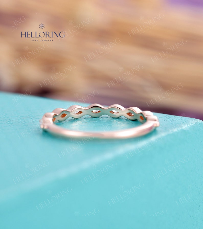 May include: A delicate gold band with a row of marquise-shaped gemstones. The band is set on a light blue background.