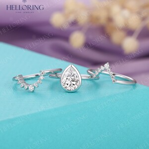 May include: Three silver rings with clear pear-shaped and round gemstones. The rings are on a turquoise surface.