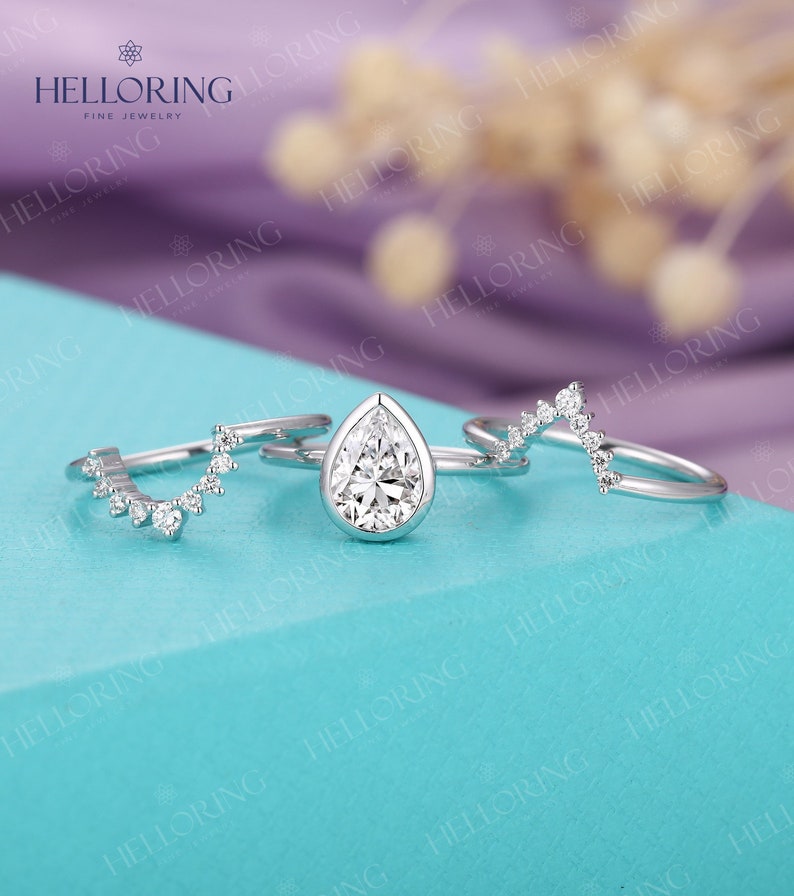 May include: Three silver rings with clear pear-shaped and round gemstones. The rings are on a turquoise surface.