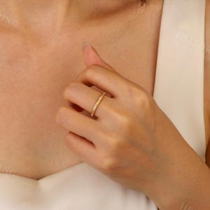 May include: A thin gold band ring with small clear stones set in the band. The ring is on a person's finger.