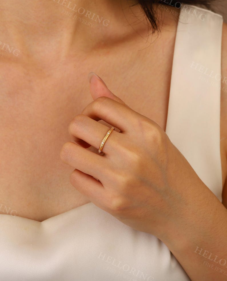 May include: A thin gold band ring with small clear stones set in the band. The ring is on a person's finger.