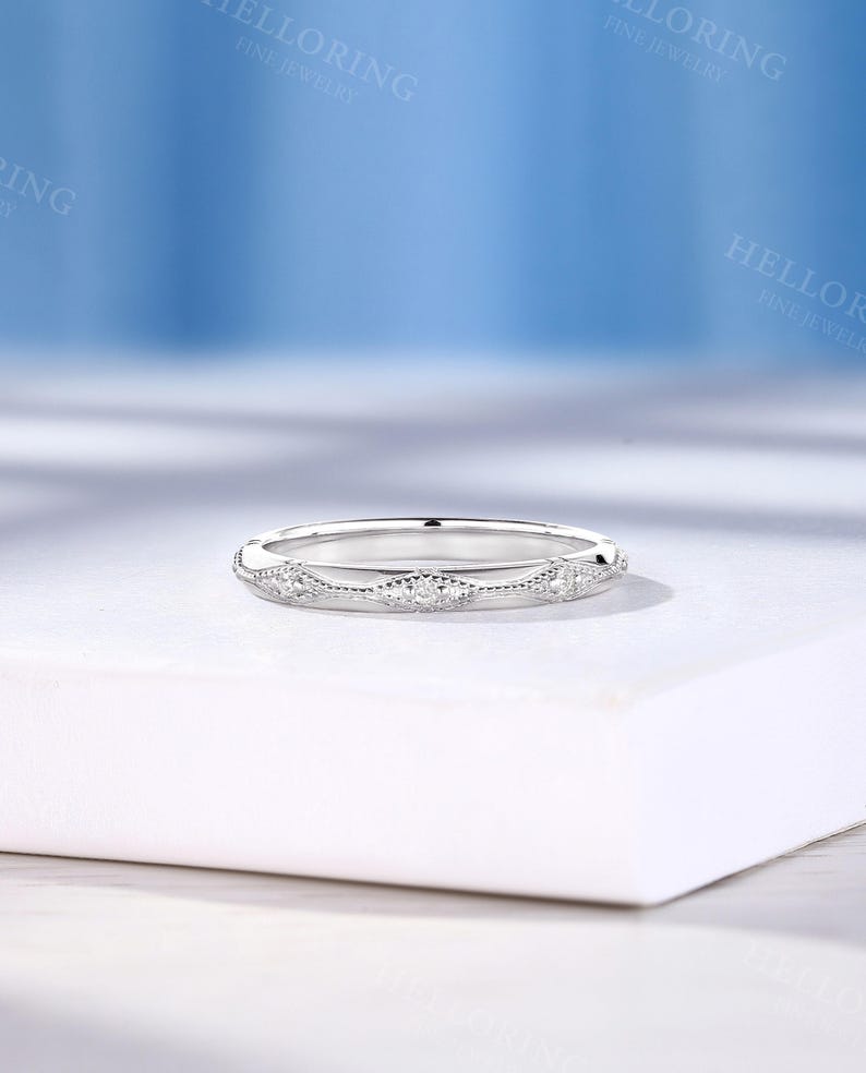 May include: A silver-toned band ring featuring a series of repeating marquise-shaped motifs along the outer surface. Each motif is accented with small, clear, round-cut stones and bordered by delicate milgrain detailing along the edges.