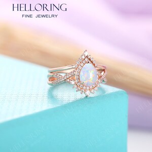 May include: A pear-shaped opal engagement ring set in rose gold with a halo of smaller diamonds. The ring is part of a three-piece set, with a matching band on either side.