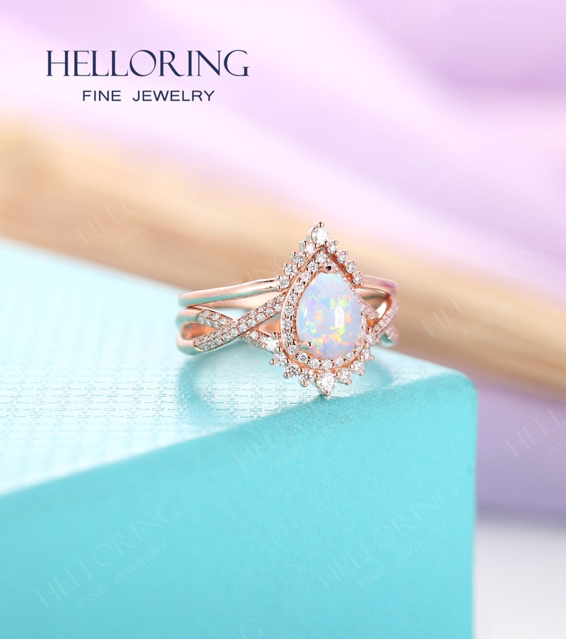 May include: A pear-shaped opal engagement ring set in rose gold with a halo of smaller diamonds. The ring is part of a three-piece set, with a matching band on either side.