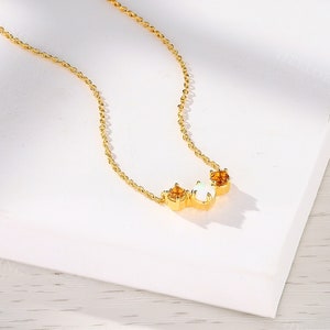 May include: A gold chain necklace with a delicate pendant featuring three stones: two small orange stones and one larger white stone.