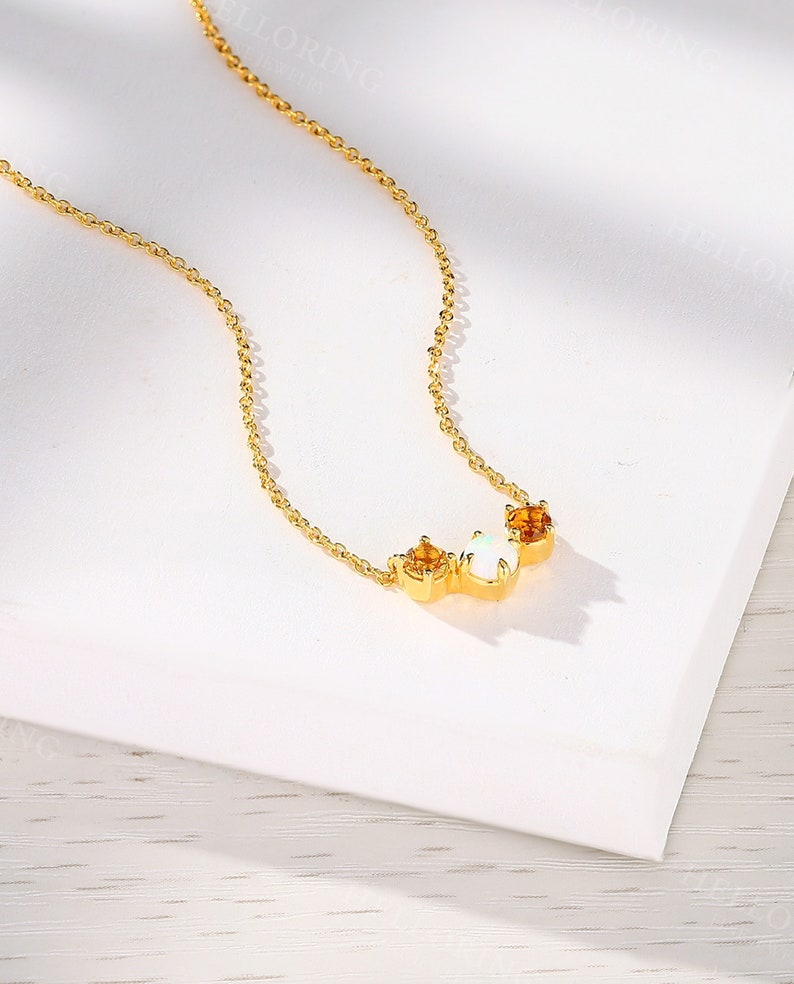 May include: A gold chain necklace with a delicate pendant featuring three stones: two small orange stones and one larger white stone.
