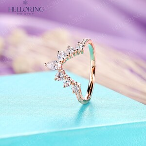 May include: A rose gold ring with a delicate, V-shaped design featuring a row of small round diamonds and a cluster of pear-shaped diamonds.