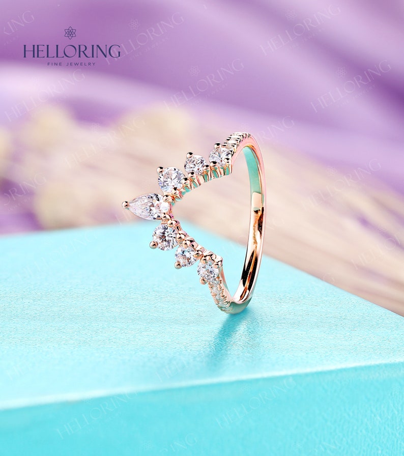 May include: A rose gold ring with a delicate, V-shaped design featuring a row of small round diamonds and a cluster of pear-shaped diamonds.