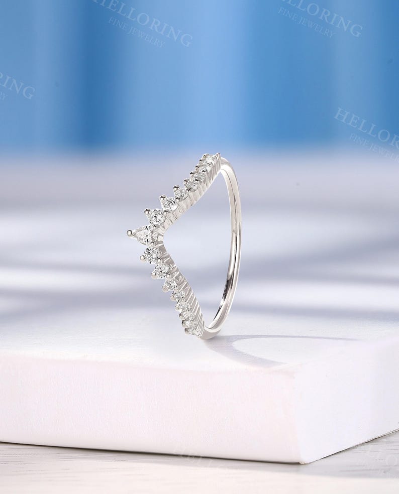 May include: A silver ring with a V-shaped band of small, clear stones. The ring is on a white surface.