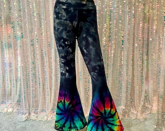 May include: Black and gray tie-dye flare pants with a high waist. The bottom flares feature a vibrant spiral tie-dye design in shades of red, orange, yellow, green, blue, and purple. The pants are made of a stretchy material.