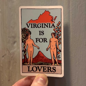 May include: A rectangular sticker with the text "VIRGINIA IS FOR LOVERS" and an illustration of two nude figures, a mountain, and the state outline in red. The background is light blue.