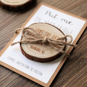 May include: A wooden save the date card with a rustic wood slice attached. The wood slice has the text "Save the Date" and the date "10/28/17" engraved on it. The card also has the text "Put me on your fridge" and "Formal invitation to follow".