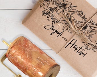 Könnte beinhalten: Eine Holz-Teigrolle mit floralem Design und ein Paket, das in braunes Papier gewickelt und mit Bindfaden verschnürt ist. Das Paket hat eine Blumenillustration und die Namen "Sujadi and Hartini" aufgedruckt.