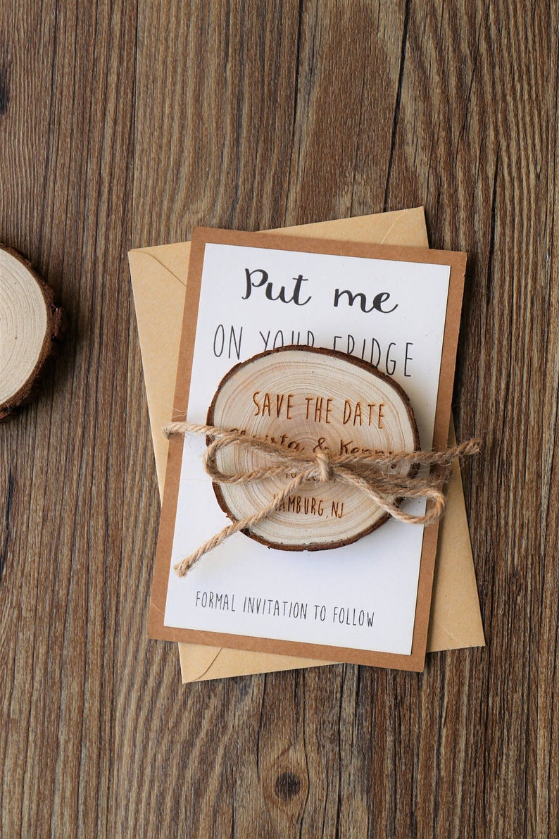 May include: A white card with the text "Put me on your fridge" and "Save the Date" with a wooden circle attached with twine. The wooden circle has the text "Christa & Kenny" and "Hamburg, NJ". The card also has the text "Formal Invitation to Follow".