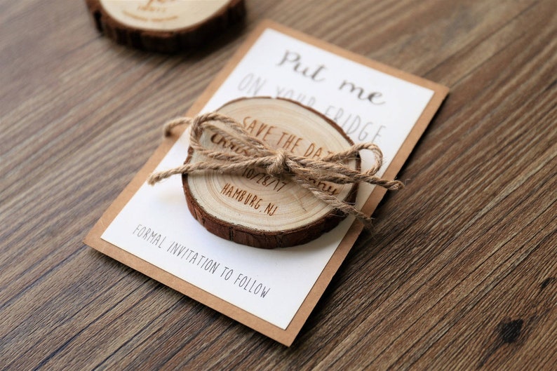 May include: A wooden save the date card with a rustic wood slice attached. The wood slice has the text "Save the Date" and the date "10/28/17" engraved on it. The card also has the text "Put me on your fridge" and "Formal invitation to follow".