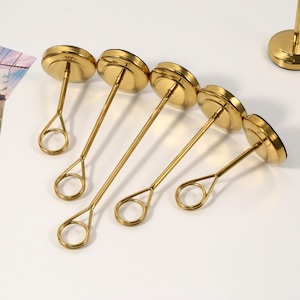 May include: A collection of gold-colored metal photo holders. Each holder has a circular base, a slender stem, and a circular top. The holders are arranged on a white surface, with a photo in the background.