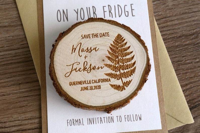 Puede incluir: Un im&aacute;n de madera para guardar la fecha con un dise&ntilde;o de helecho. El im&aacute;n dice "Save the Date" y "Mossu + Fickson" con la fecha "June 20, 2020" y la ubicaci&oacute;n "Guerneville, California".