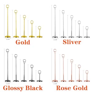May include: A collection of metal table number holders in gold, silver, glossy black, and rose gold. Each set includes five holders of varying heights, with a circular ring at the top for holding cards. The base of each holder is 5.1 cm in diameter.