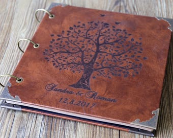 May include: Brown leather photo album with a tree design and the names Sandra & Roman and the date 12.8.2017 embossed on the cover. The album has metal rings and corner accents.