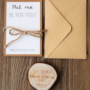 May include: A rustic save the date card with a wooden slice featuring the text "Save the Date, Christa & Kenny, 10/28/17, Hamburg NJ". The card is accompanied by a kraft paper envelope and a white card with the text "Put me on your fridge, Formal invitation to follow".