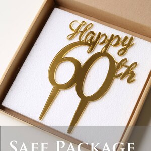 May include: Gold mirror acrylic cake topper with the words "Happy 60th" in a cursive font. The topper is packaged in a white foam box.