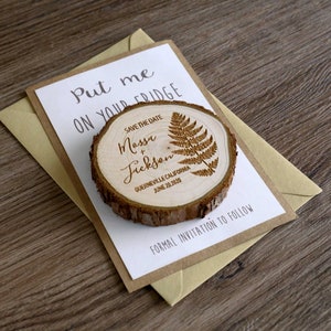 Puede incluir: Im&aacute;n para guardar la fecha con un dise&ntilde;o de rodaja de madera. El im&aacute;n presenta un dise&ntilde;o de helecho y el texto "Save the Date Massi & Jickson, Guerneville, California, 20 de junio de 2020". El im&aacute;n est&aacute; en una tarjeta blanca con el texto "Put me on your fridge" y un sobre marr&oacute;n.
