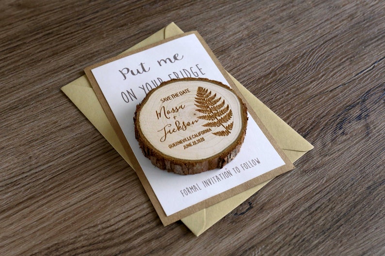 Puede incluir: Im&aacute;n para guardar la fecha con un dise&ntilde;o de rodaja de madera. El im&aacute;n presenta un dise&ntilde;o de helecho y el texto "Save the Date Massi & Jickson, Guerneville, California, 20 de junio de 2020". El im&aacute;n est&aacute; en una tarjeta blanca con el texto "Put me on your fridge" y un sobre marr&oacute;n.