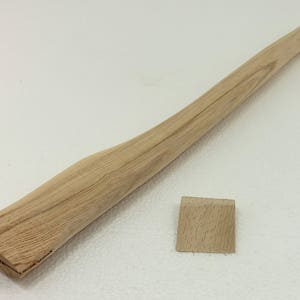 Può includere: Un manico di ascia in legno con finitura naturale. Il manico è in legno chiaro con una superficie liscia. Il manico è lungo circa 76 cm e presenta una leggera curvatura. Il manico è mostrato con un piccolo cuneo di legno.