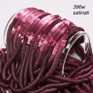 Könnte beinhalten: Nahaufnahme einer Sammlung von weinroten und rosa Pailletten, die aus einem transparenten Glasbehälter quellen. Die Pailletten sind in Strängen angeordnet, mit einem Farbverlauf von dunklem Weinrot zu hellem Rosa. Der Text oben rechts lautet "396w satinati."