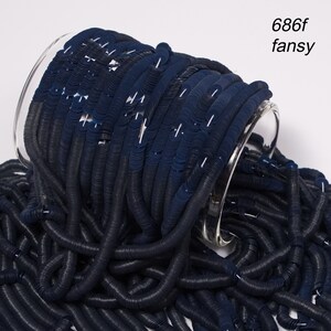 May include: A spool of dark blue sequins, spilling out of a clear glass jar. The sequins are small and round, and they have a metallic sheen.