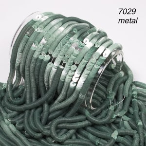 Könnte beinhalten: Grüne Metallpailletten fallen aus einem transparenten Glasbehälter. Die kreisförmigen Pailletten sind aufgereiht und erzeugen ein strukturiertes, fließendes Aussehen. Der Text "7029 metal" ist sichtbar. Geeignet für Bastelarbeiten.